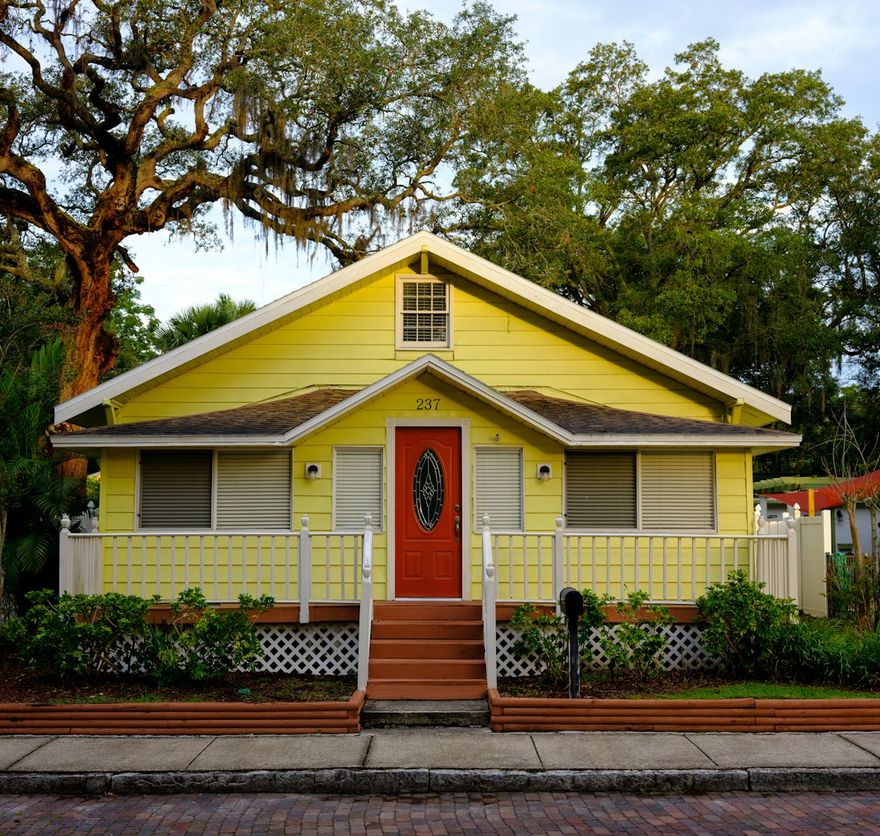 Yellow Lowcountry cottage with a red door beneath a live oak