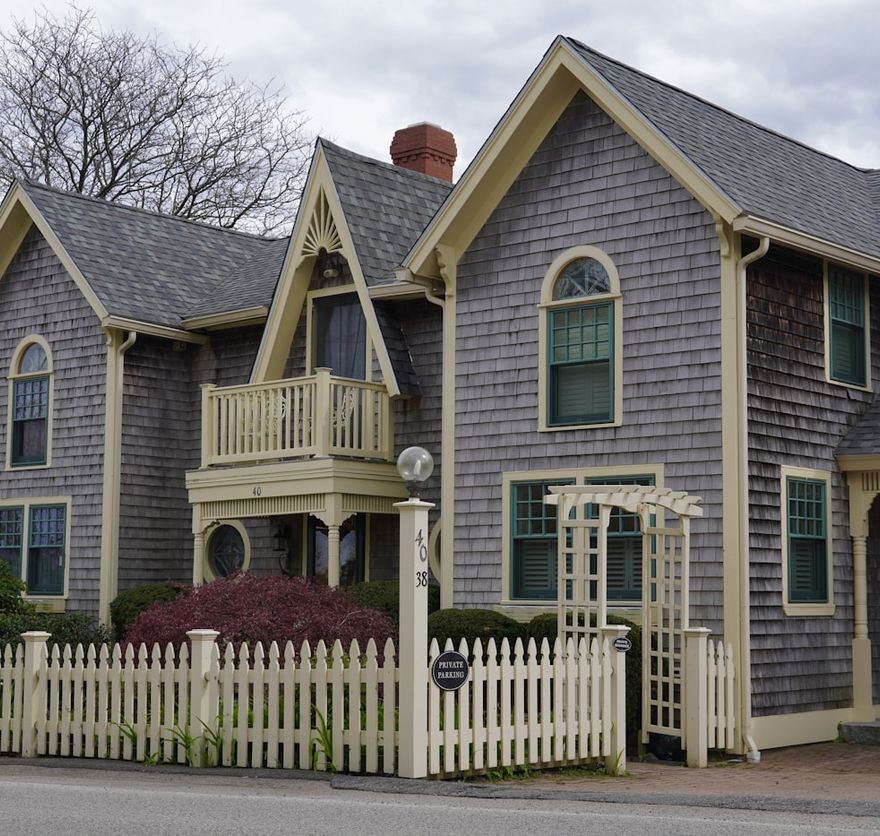Grey-shingled village cottage with cream trim and a white picket fence