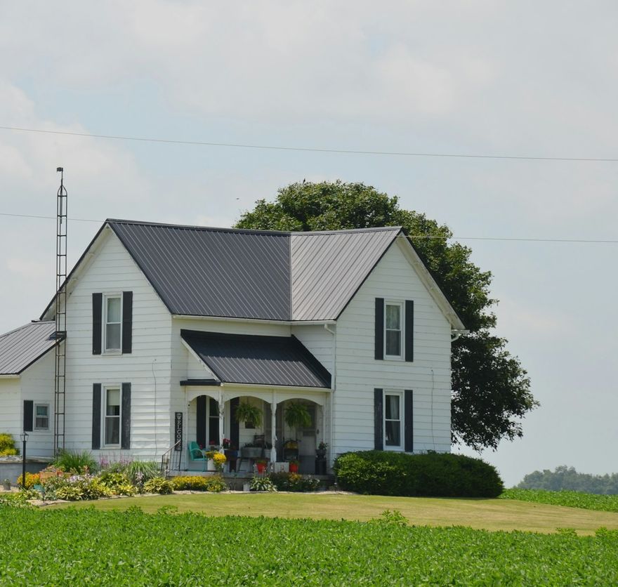 White farmhouse with a standing-seam metal roof on an open green acre